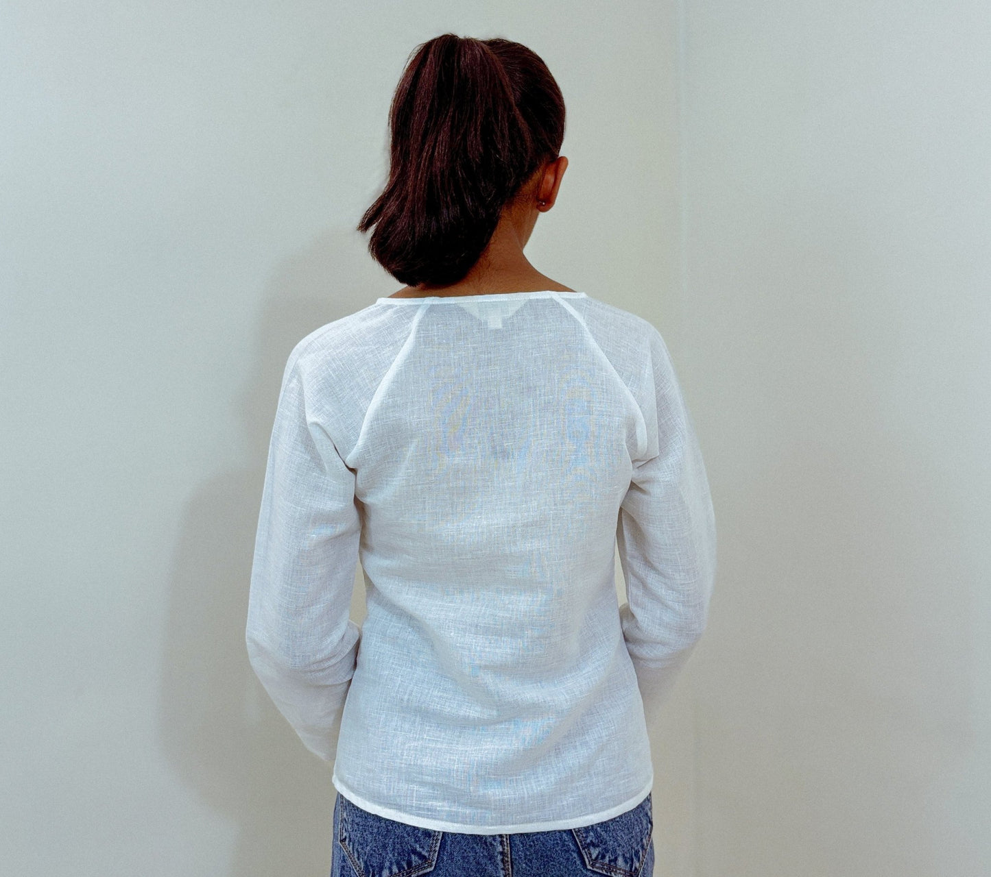 Back view of white Zen blouse showcasing pleat details in studio